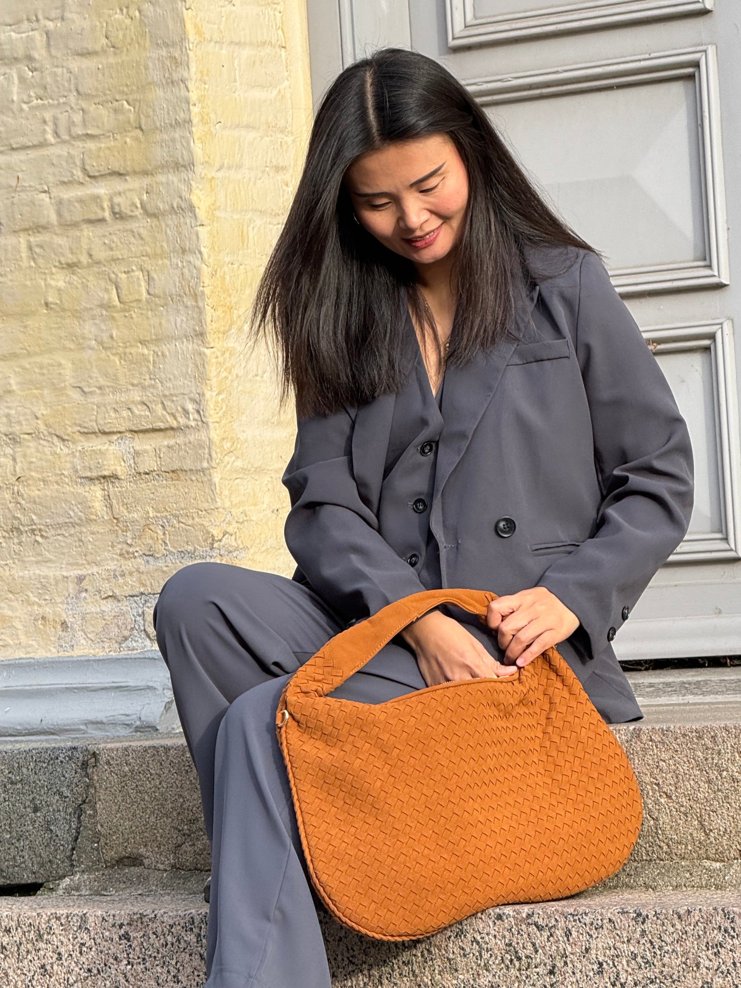 Model holder Anna Fake Suede flettet skuldertaske i brun fra MAS SELECTION i den ene hånd