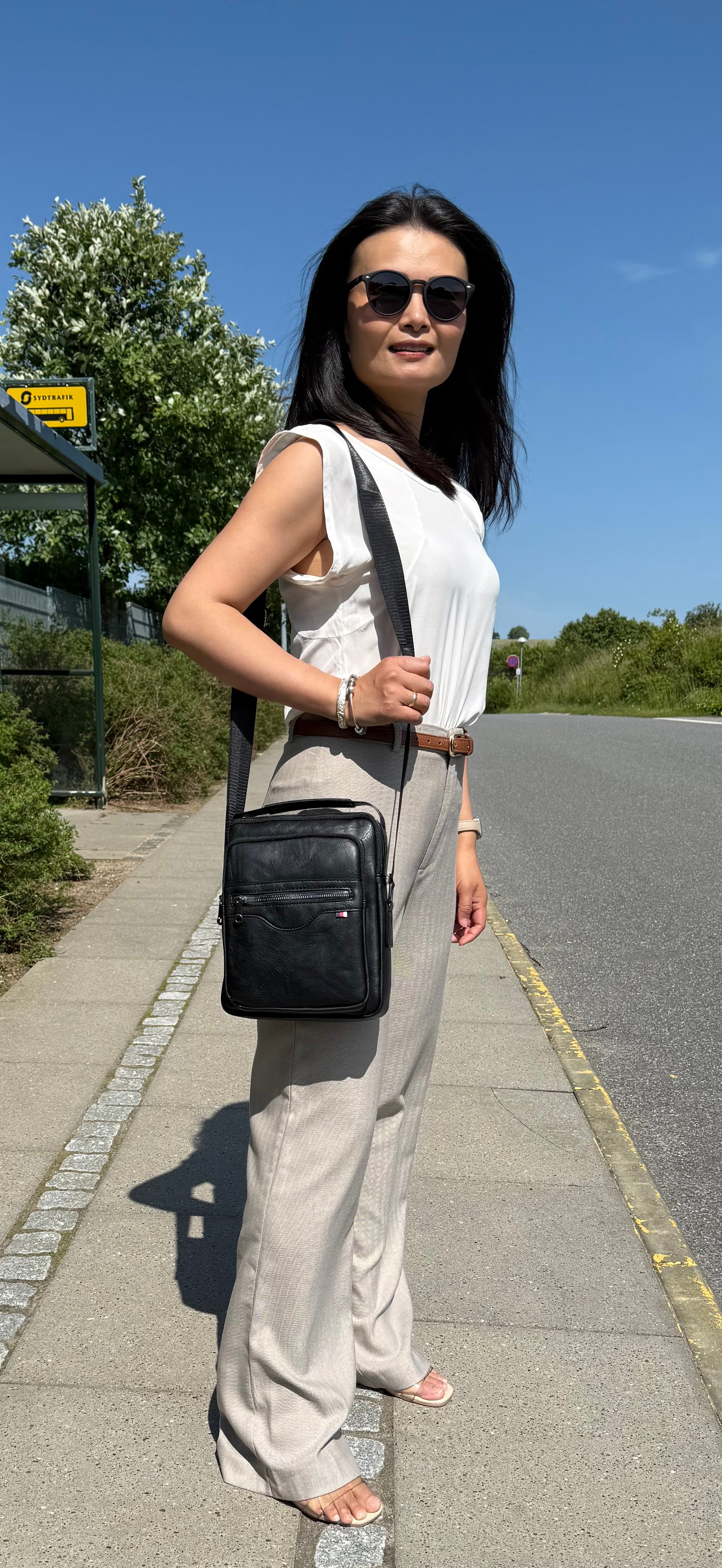 Kvindelig model bærer Unisex Messenger Taske i sort over skulderen.