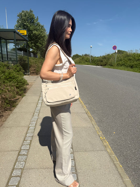 Model med Asta skuldertaske i beige over skulderen, som viser taskens størrelse.