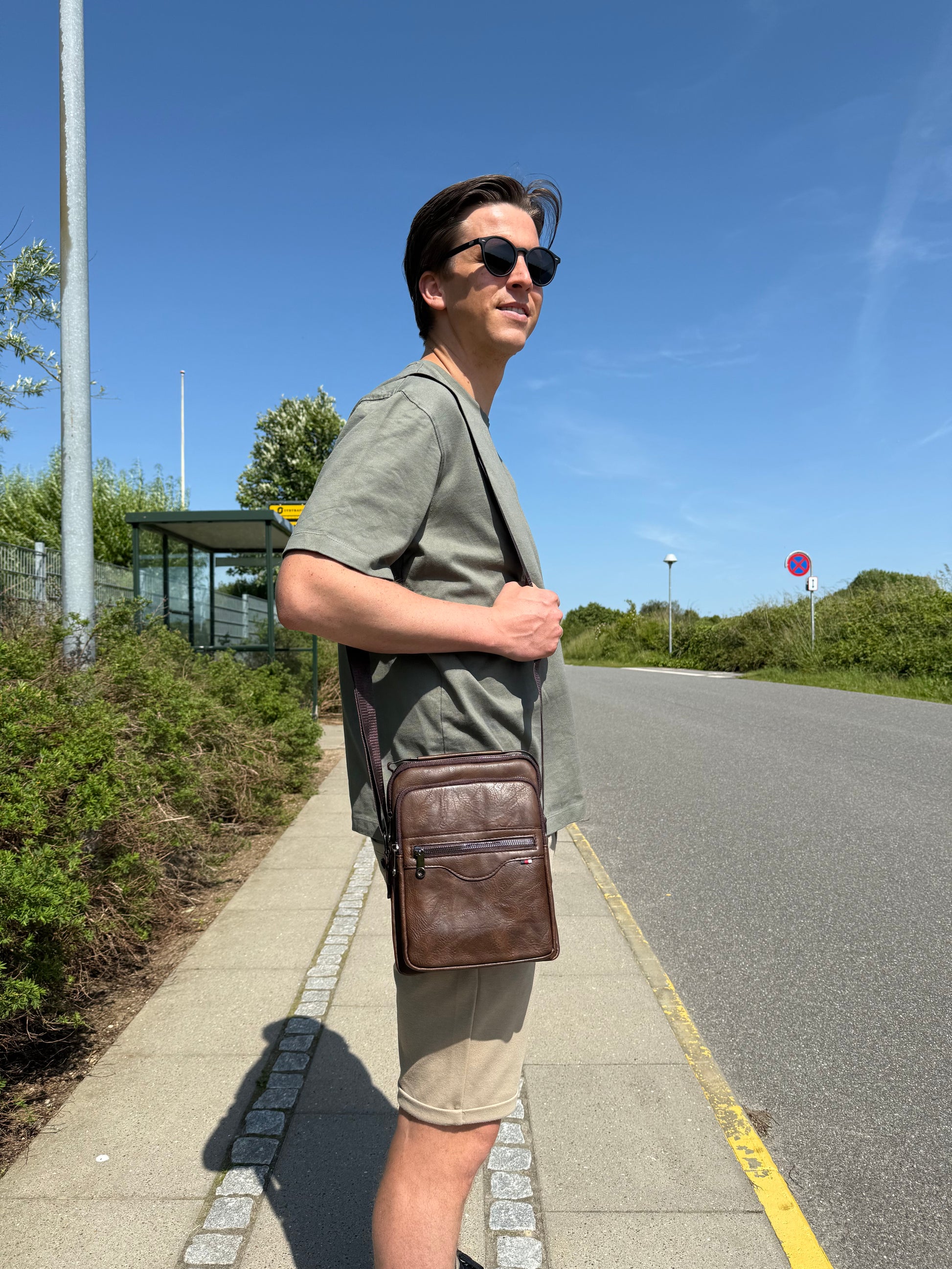 Mandlig model bærer Unisex Messenger Taske i mørkebrun over skulderen.