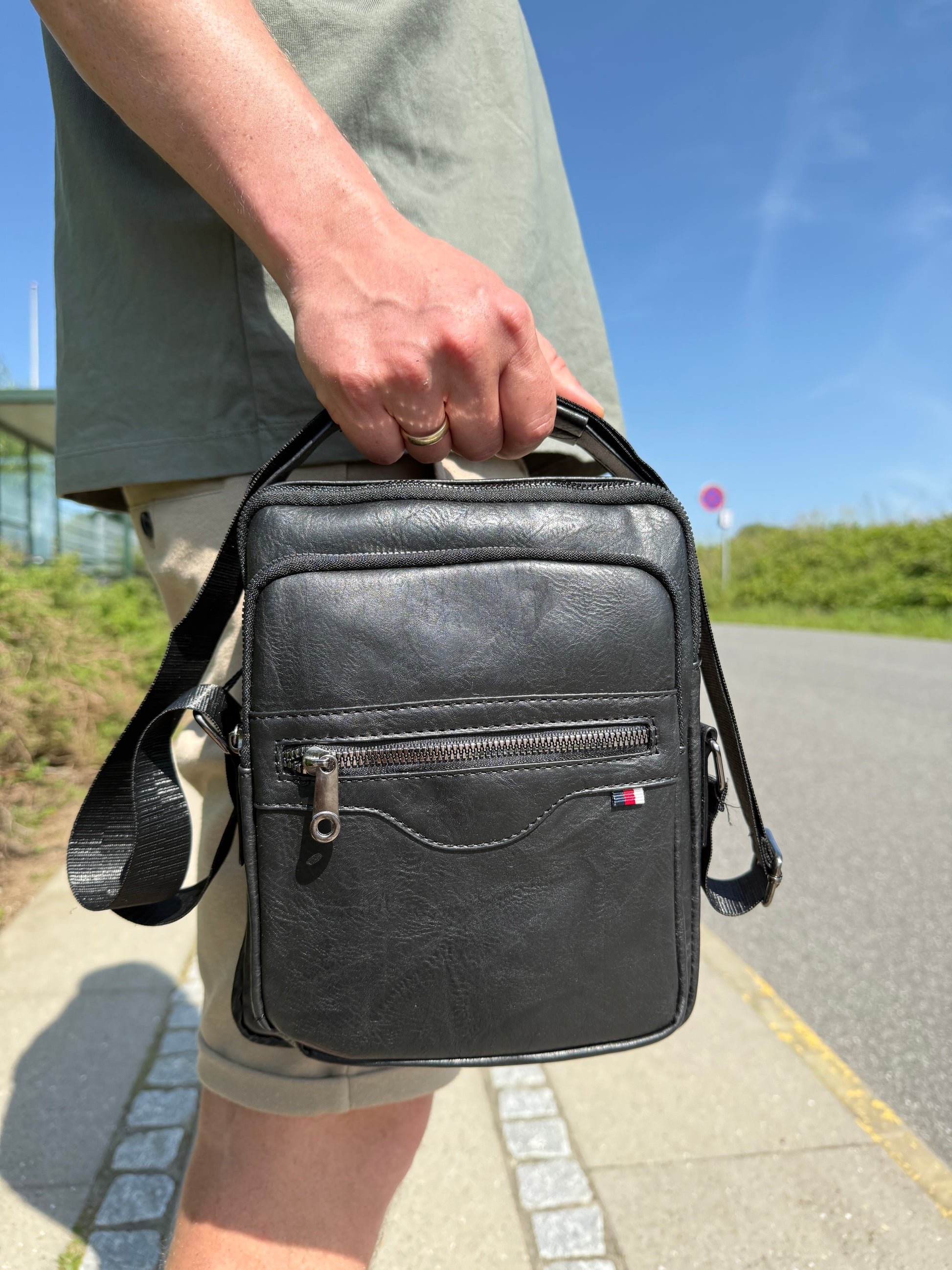 Mandlig model holder Unisex Messenger Taske i sort i hånden.